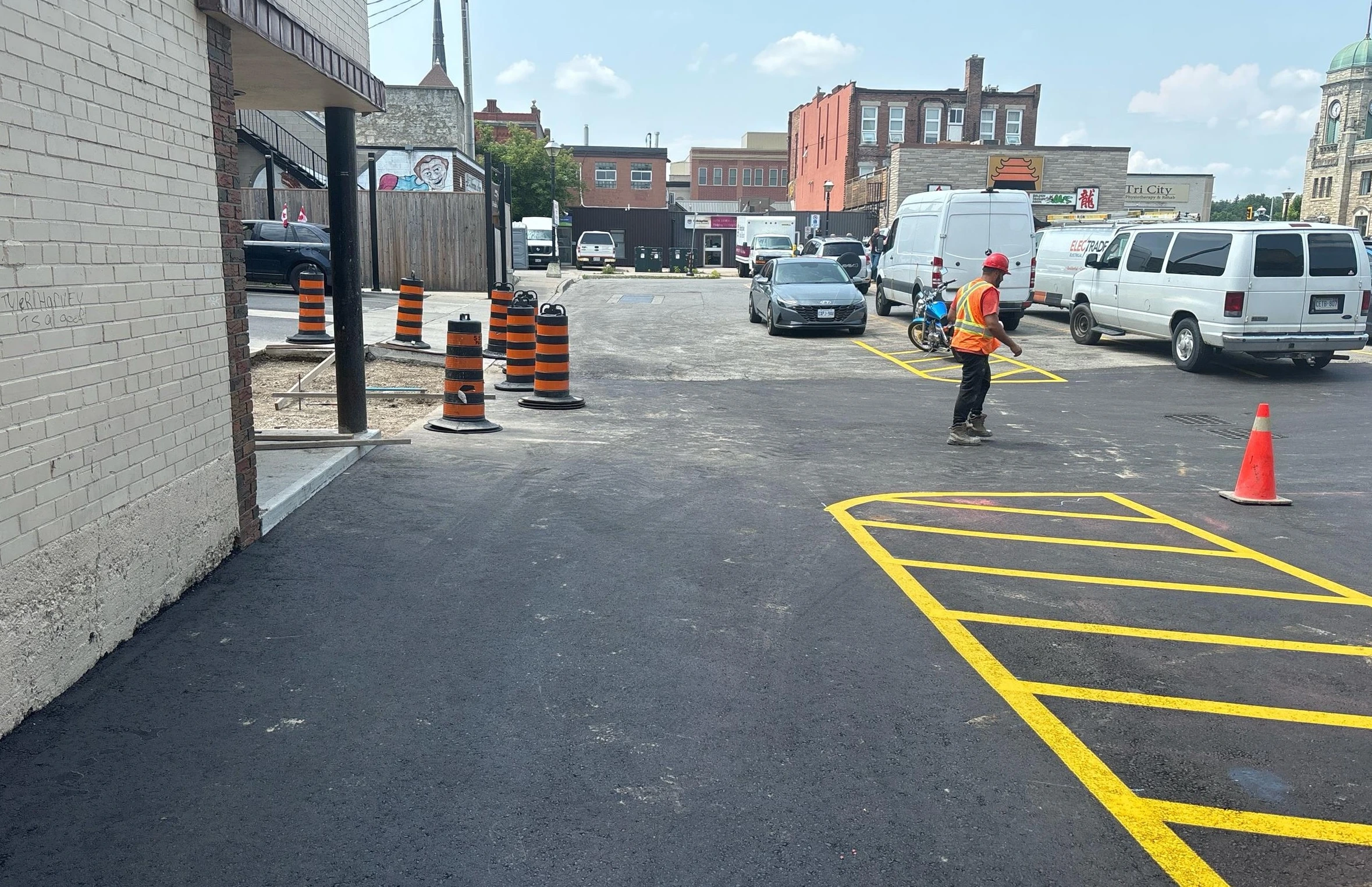 Dickson St Lot Storm Improvement (Construction) - Newly paved parking lot with yellow line markings and construction worker